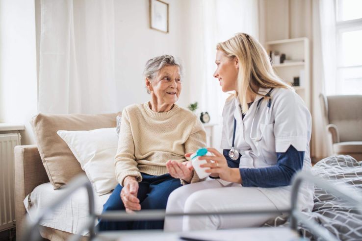 Ärztin sitzt mit einer Patientin am Bett reicht ihr Medikamente