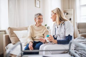 Ärztin sitzt mit einer Patientin am Bett reicht ihr Medikamente