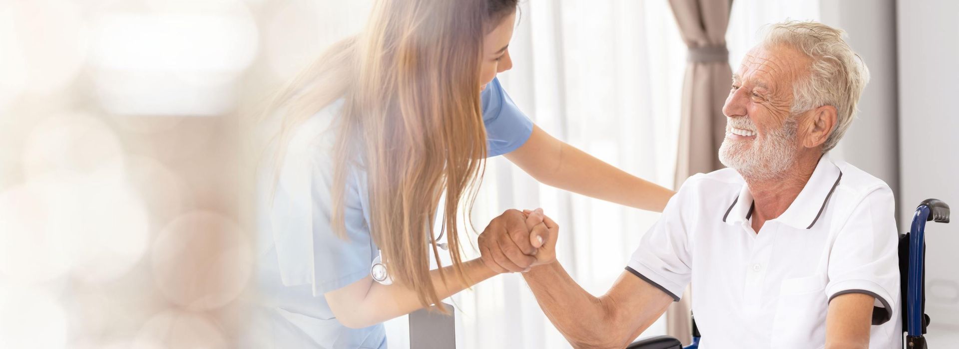 Pflegerin hält die Hand eines älteren Mannes im Rollstuhl