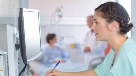 Eine Pflegerin sitzt am Computer und macht Notizen auf einem Block