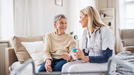 Ärztin sitzt mit einer Patientin am Bett reicht ihr Medikamente