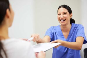 Eine Pflegerin reicht lächelnd einem Patienten ein Formular und einem Stift