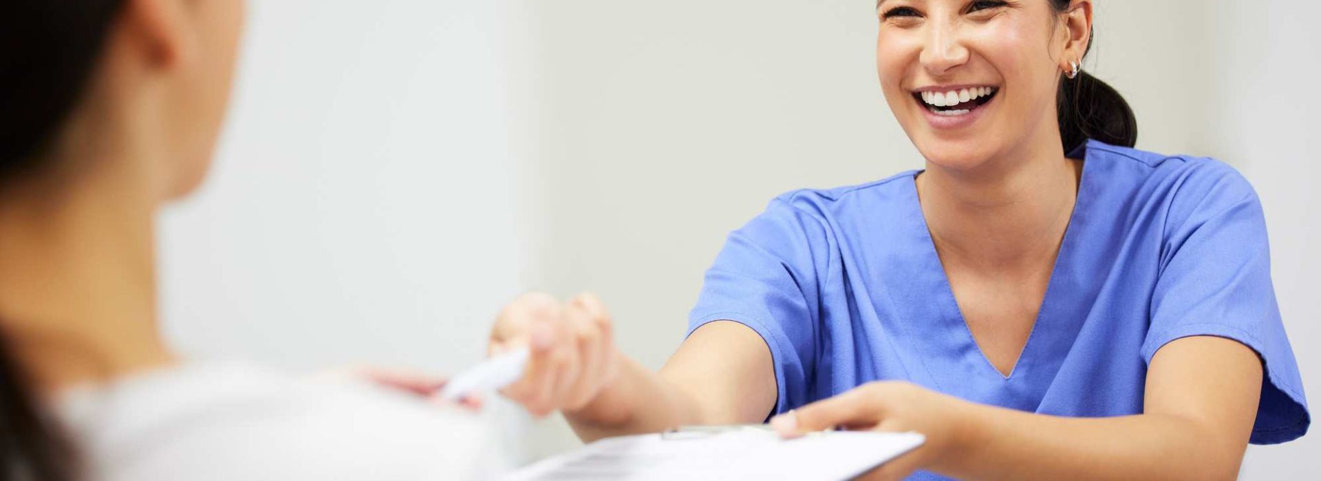 Eine Pflegerin reicht lächelnd einem Patienten ein Formular und einem Stift