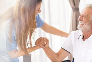 Pflegerin hält die Hand eines älteren Mannes im Rollstuhl