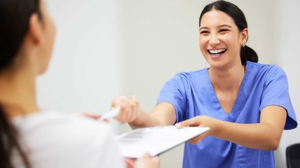 Eine Pflegerin reicht lächelnd einem Patienten ein Formular und einem Stift