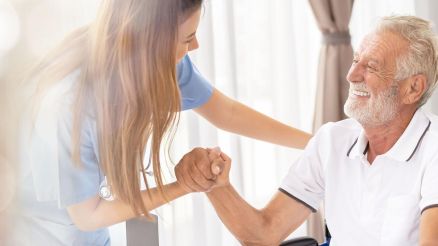 Pflegerin hält die Hand eines älteren Mannes im Rollstuhl